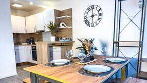 A dining table set with plates, glasses, and cutlery in a modern kitchen with white cabinets and a clock on the wall.