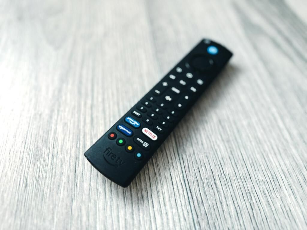 Eine schwarze Fernbedienung mit Tasten für Netflix, Fernsehen und weitere Funktionen auf einer Holzoberfläche.