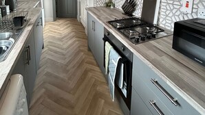 Eine moderne Küche mit Fischgrätparkett, einem Gasherd, einer Mikrowelle und grauen Schränken.