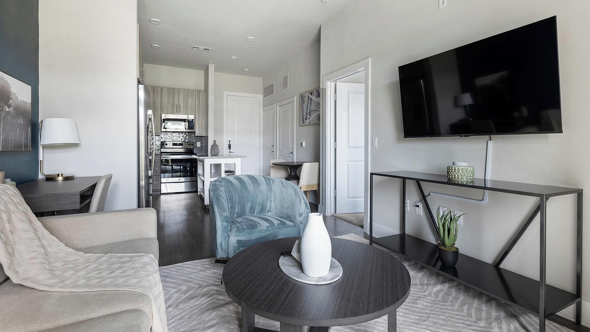 A modern living room with a sofa, a coffee table, a TV, and a dining area with a table and chairs.