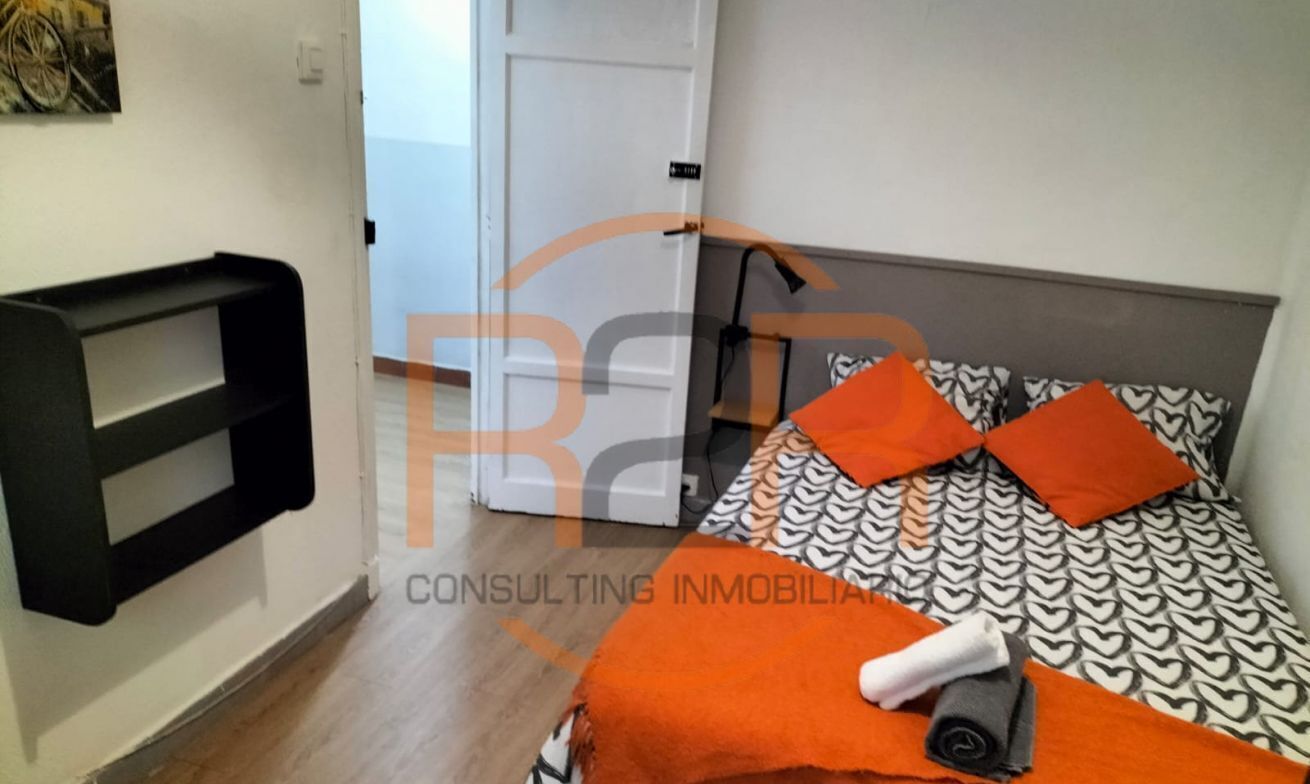 A bedroom with a bed, pillows, a bedside table, and a wall-mounted shelf.
