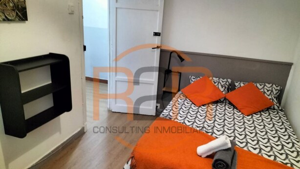 Un dormitorio con cama, almohadas, una mesita de noche y un estante en la pared.