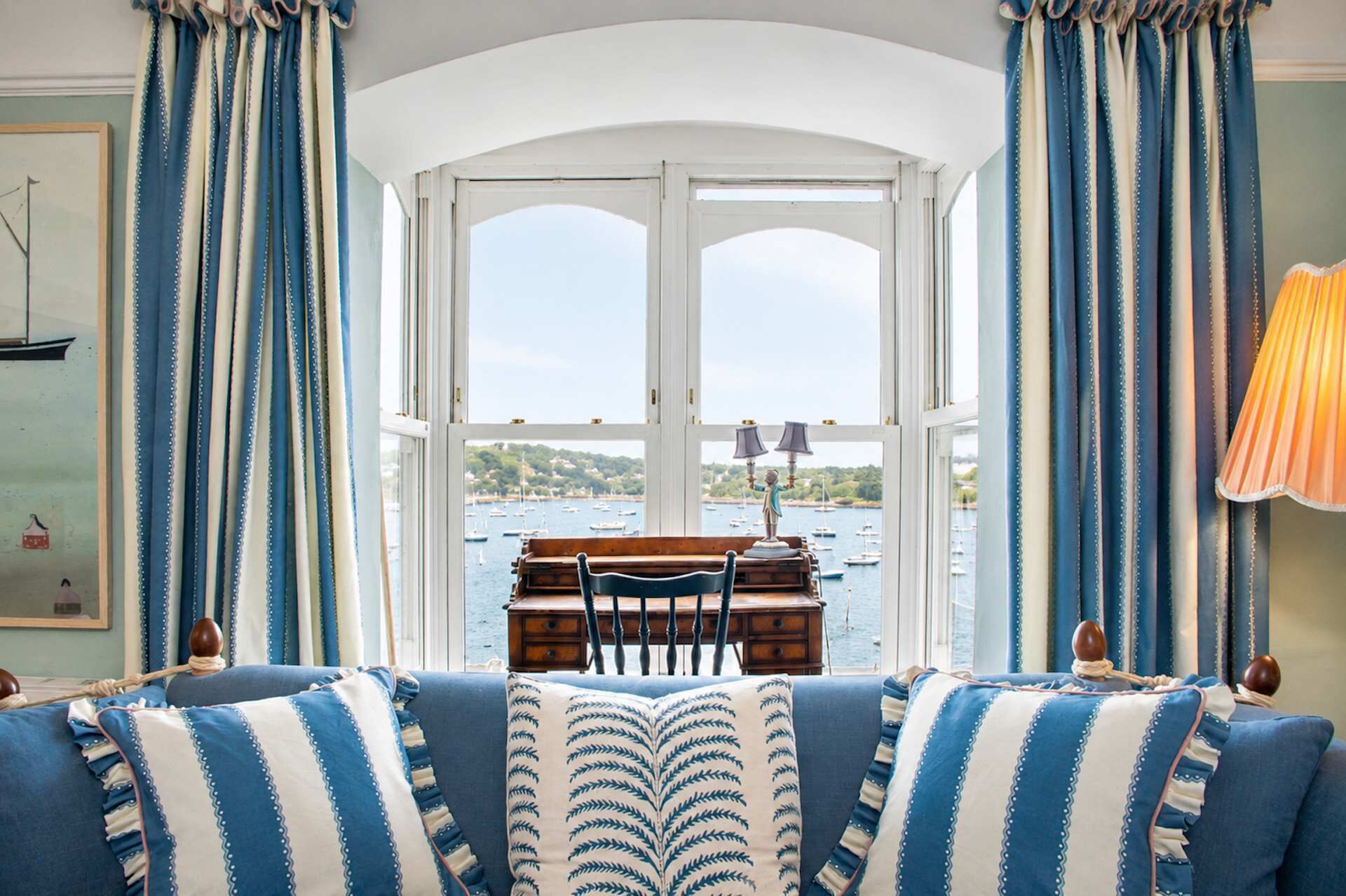 Una habitación con vista al mar, una mesa de madera con sillas y muebles a rayas azul y blanco.