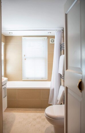 A bathroom with a toilet, a bathtub, and a window with blinds. - Chy En Glas - By Rowes Retreats (Falmouth)
