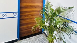 A wooden door with a blue frame and a number plate, a potted plant, and a white wall with a blue border. - Hotel Radha Ratan Inn (Jaipur)