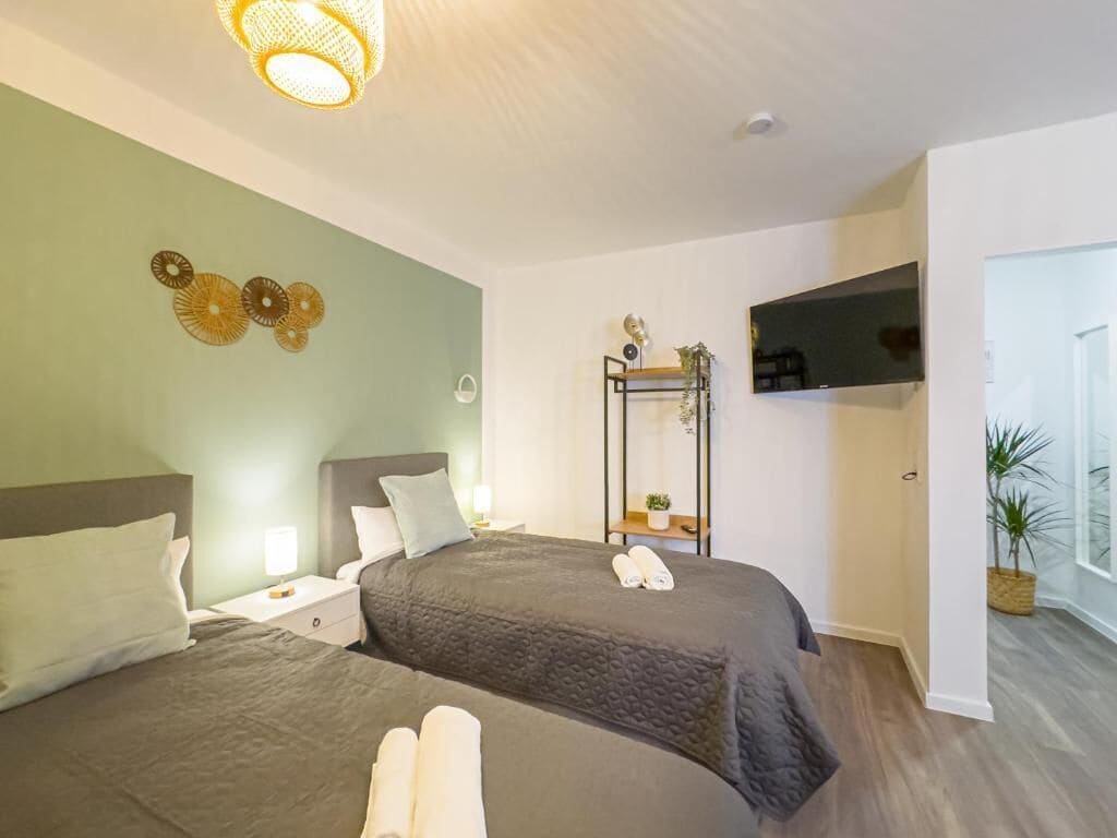 A hotel room with two beds, a TV mounted on the wall, a plant, and a door leading to another room.