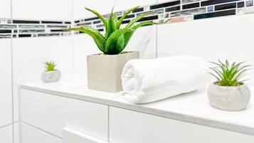 A bathroom with a white vanity, a potted aloe vera plant, a rolled white towel, and a small potted plant.