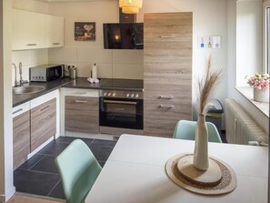 A modern kitchen with a dining table, a vase with dried plants, and a window with a view. - Saarstraße 1A (Bremen)
