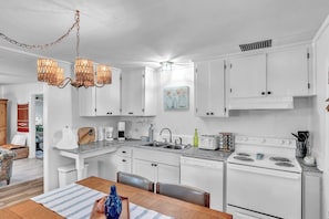 Your bright, coastal-style kitchen invites you to cook and gather, with granite counters, full appliances, and charming woven lighting overhead. - Charming Fisherman’s Cottage - Walk to Bogue Sound | DOGS OK (Cape Carteret)