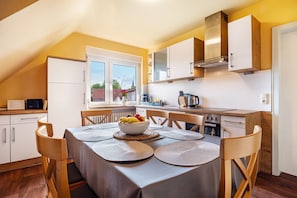 A kitchen with a dining table set for four, a bowl of fruit, and a window with a view of the outside. - Holiday Apartment 'Zum Gingko' with Balcony (Neuenkirchen)