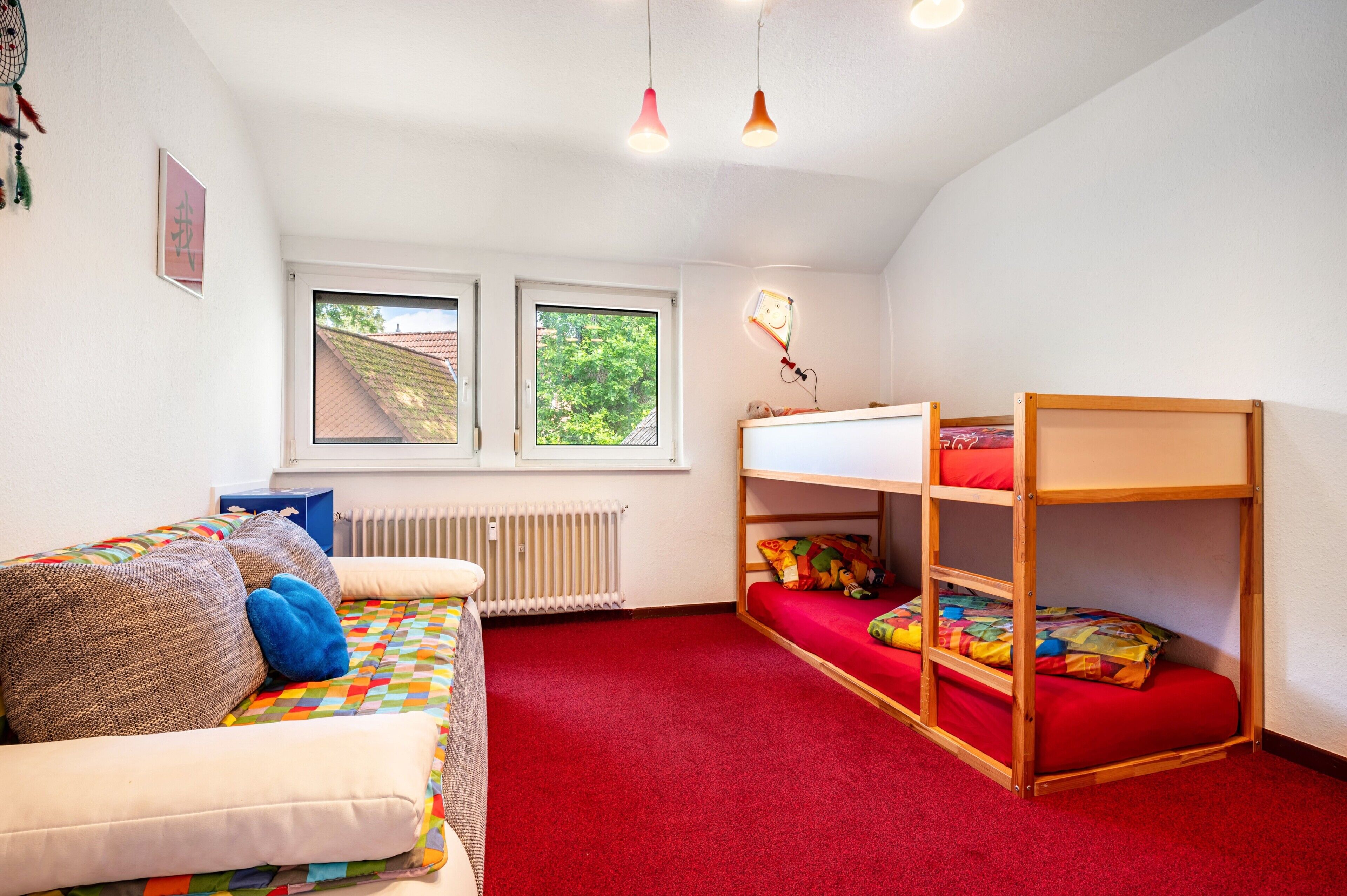 Ein Zimmer mit Etagenbett, einer Schlafcouch, einem Heizkörper und zwei Fenstern.