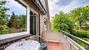 A balcony with a table and chair, a brick wall, and a view of greenery.