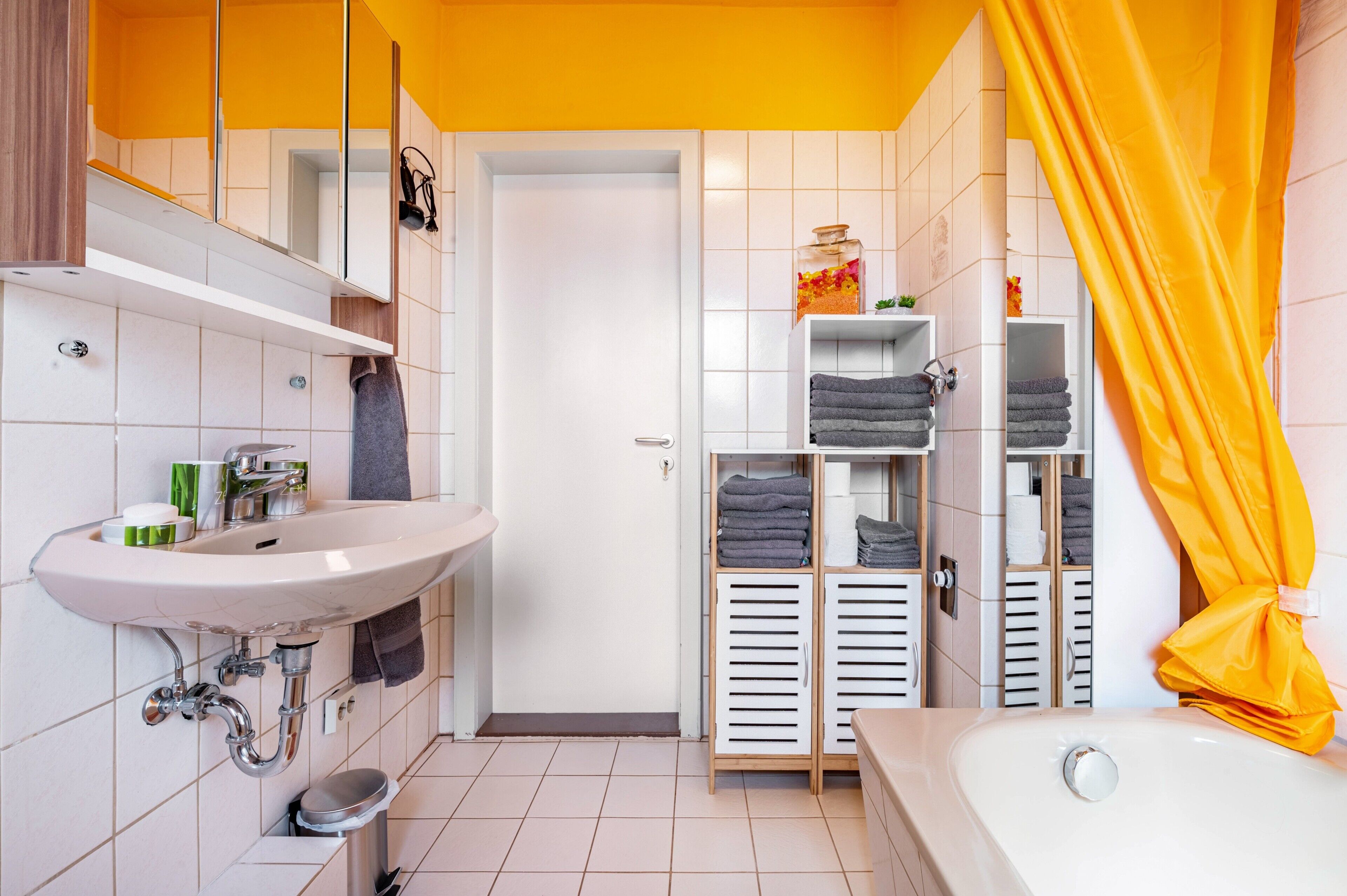 Ein Badezimmer mit Waschbecken, Spiegel, Handtuchhalter, Duschvorhang und Ablagefächern.