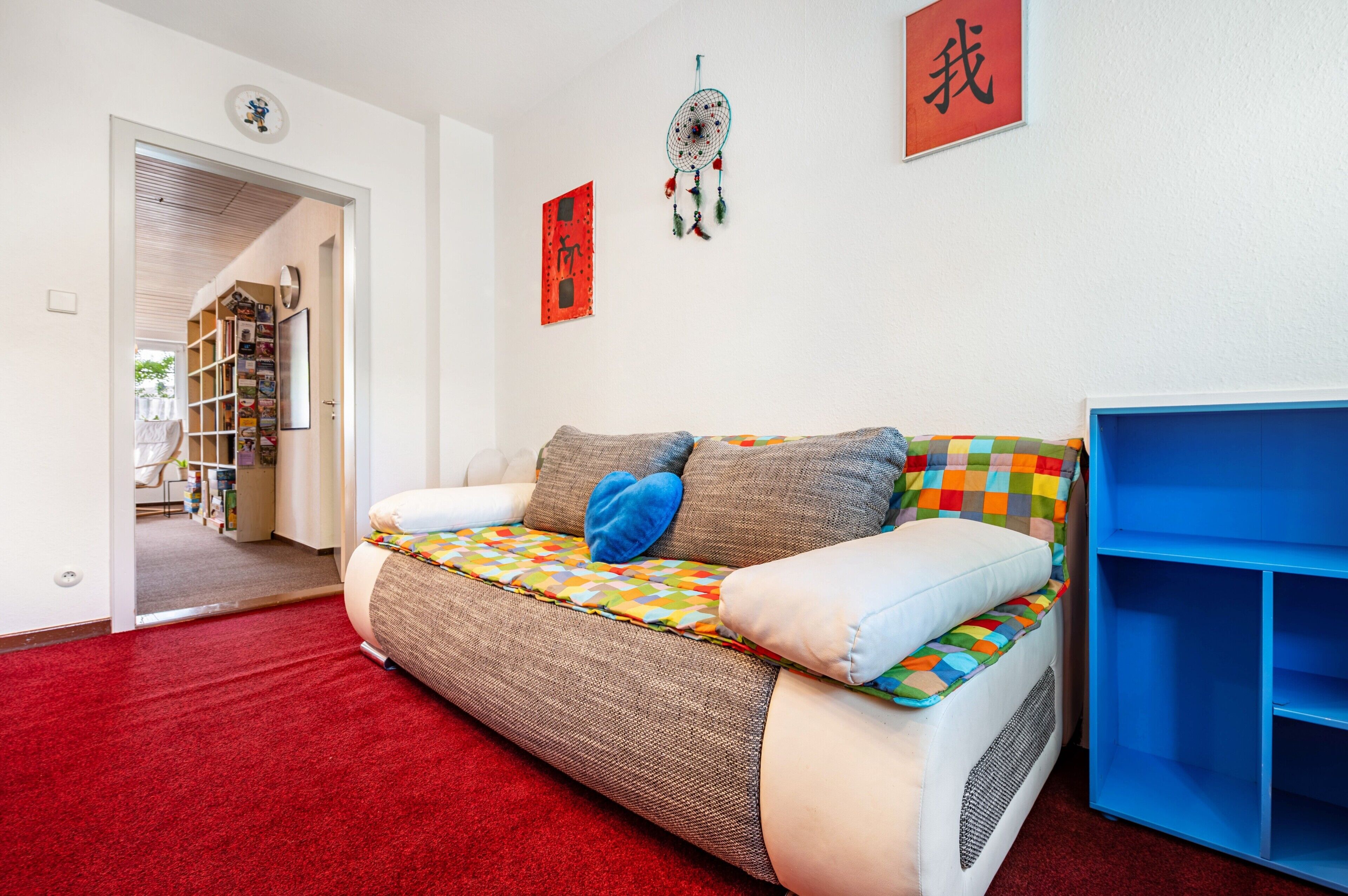 Ein gemütliches Wohnzimmer mit einer Couch, einem blauen Bücherregal und einem roten Teppich.