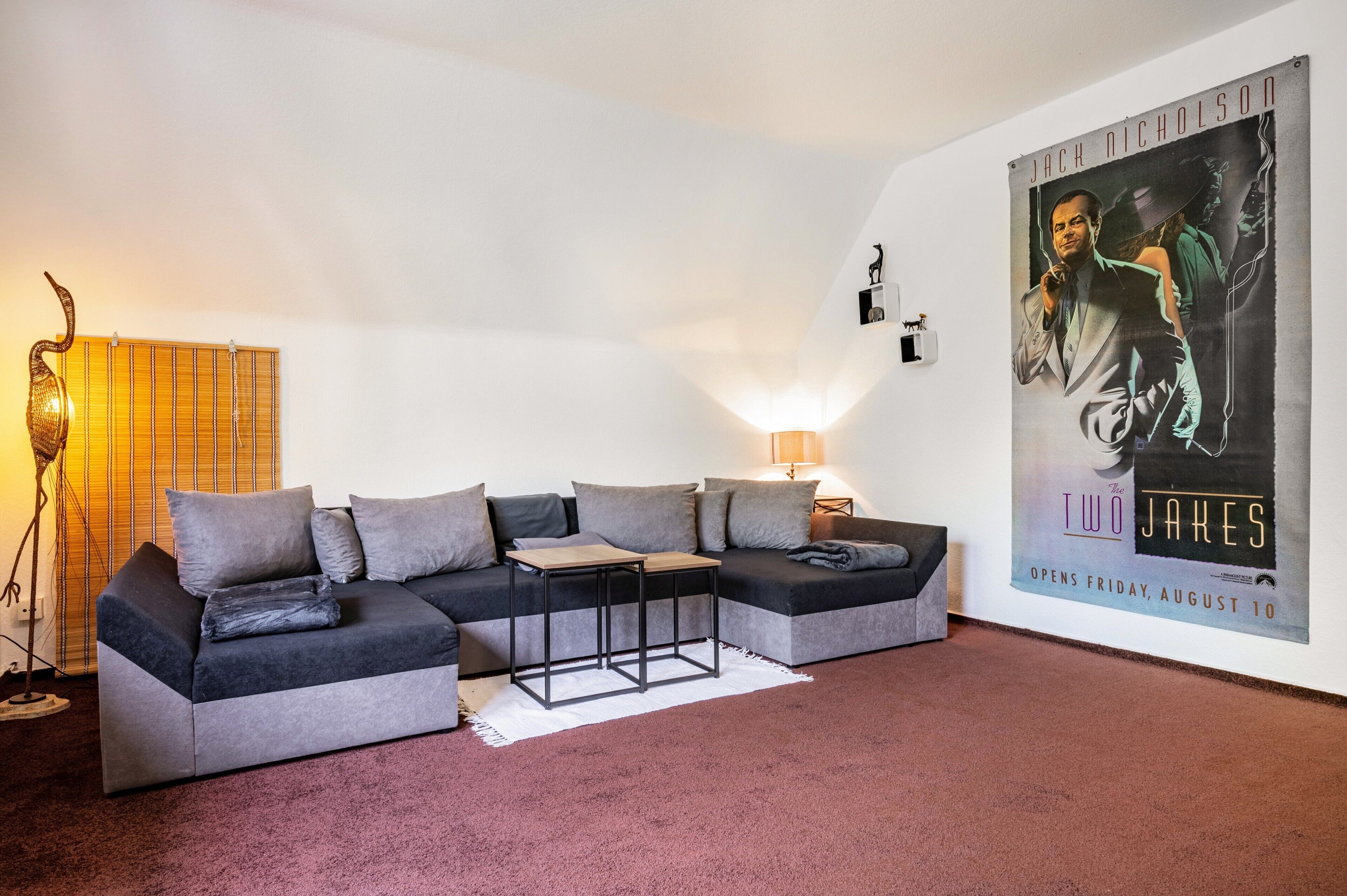 Un salon moderne avec un canapé d’angle, une petite table, un lampadaire et une affiche accrochée au mur.