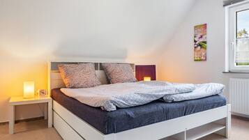Un dormitorio con cama, mesita de noche, una obra de arte en la pared y una ventana.