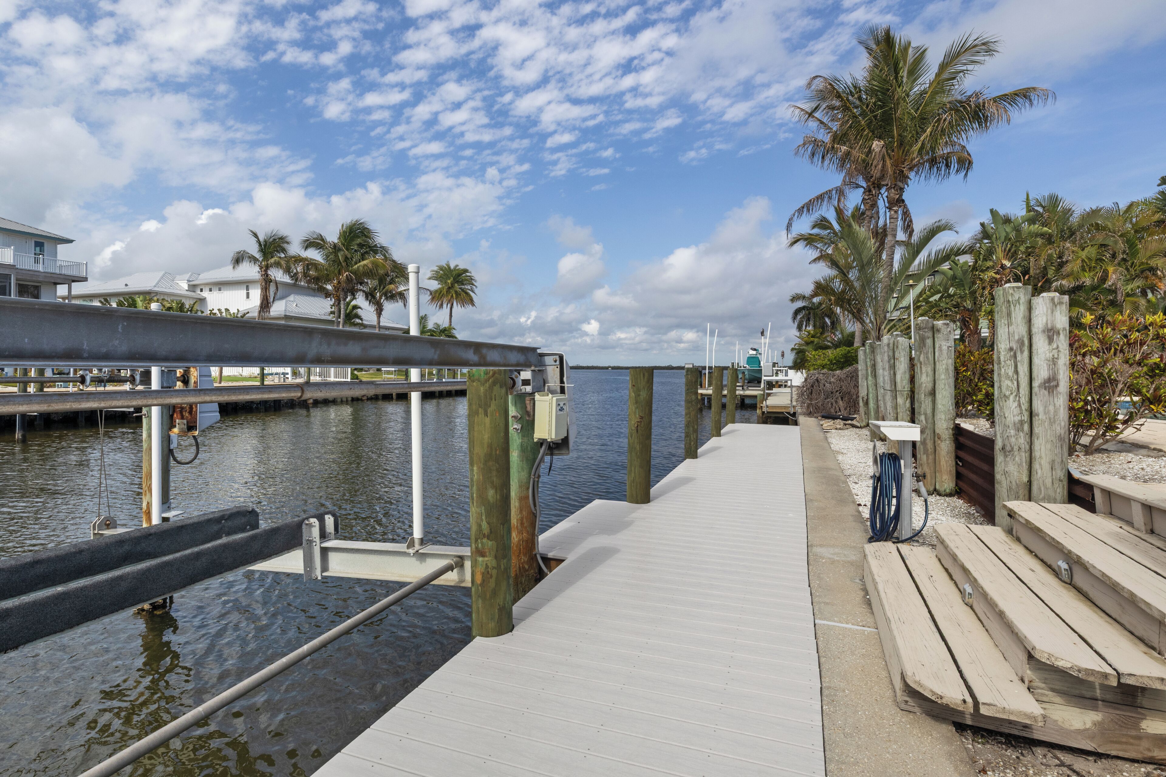A wooden dock extending into calm water, with a clear sky and palm trees in the background.