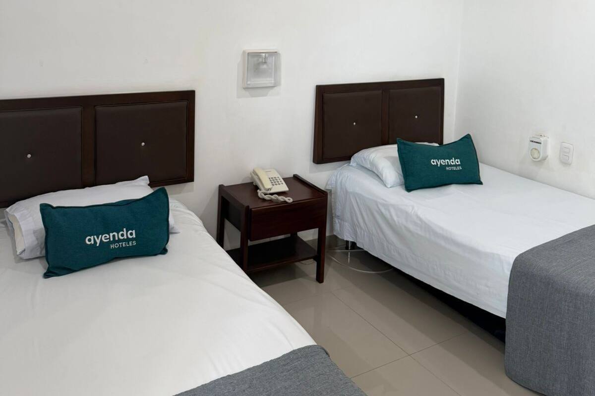 Habitación de hotel con dos camas, un ventilador de techo, teléfono en la mesita de noche y un interruptor de luz en la pared.