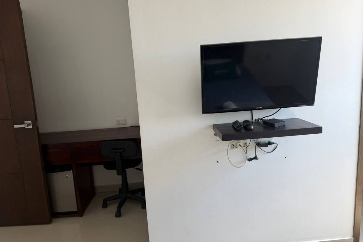 Una habitación con televisión montada, un escritorio, una silla y una puerta.