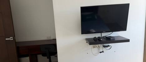 Una habitación con televisión montada, un escritorio, una silla y una puerta.