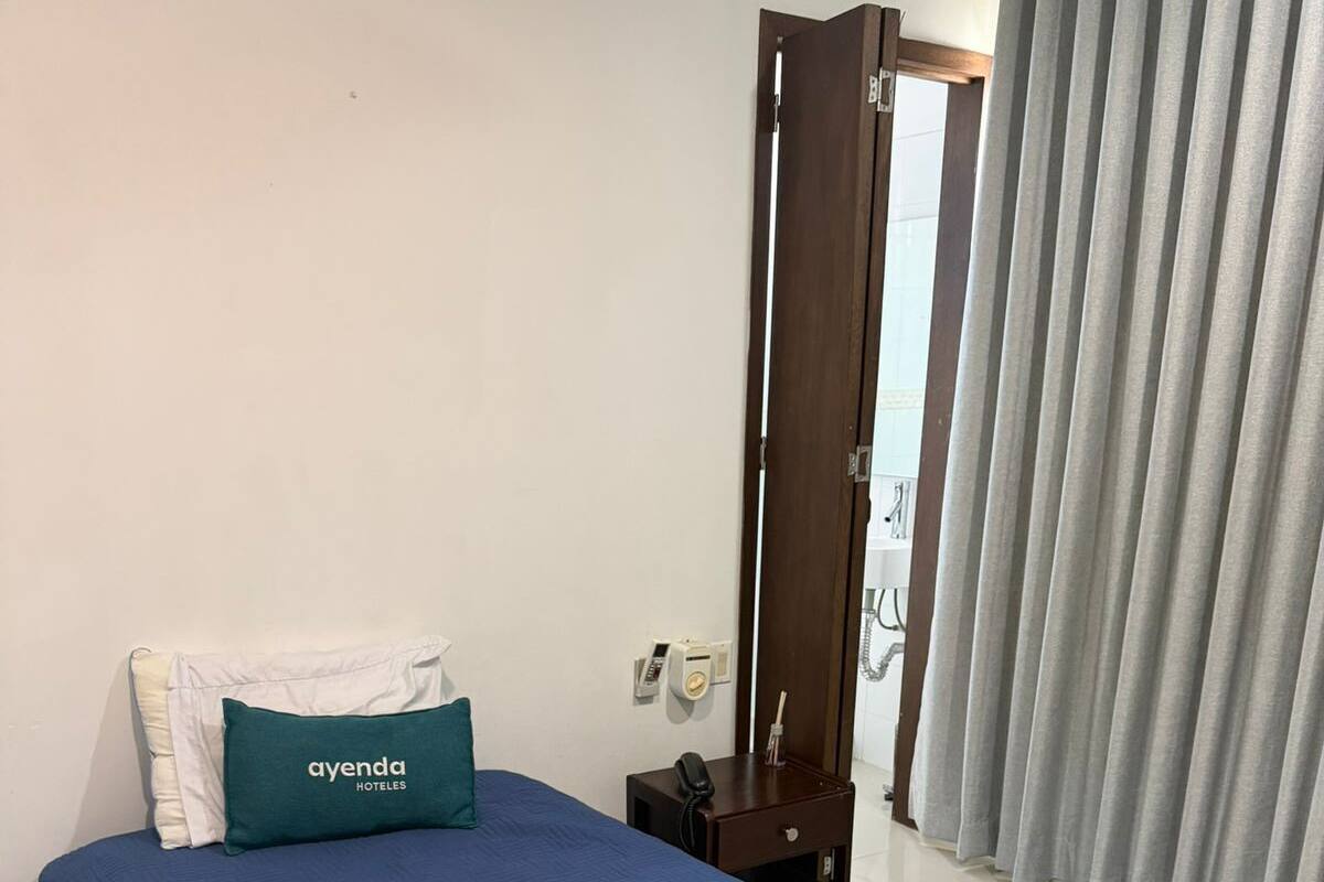 Habitación de hotel con cama, mesita de noche y teléfono, y ventana con cortinas.