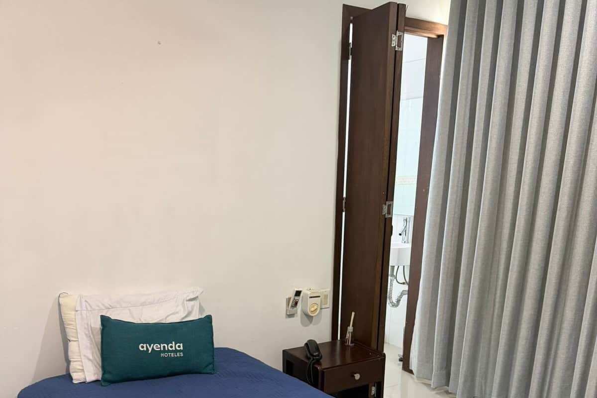 Une chambre dâhĂŽtel avec un lit, une table de chevet avec un tĂ©lĂ©phone, un rideau et un interrupteur fixĂ© au mur.