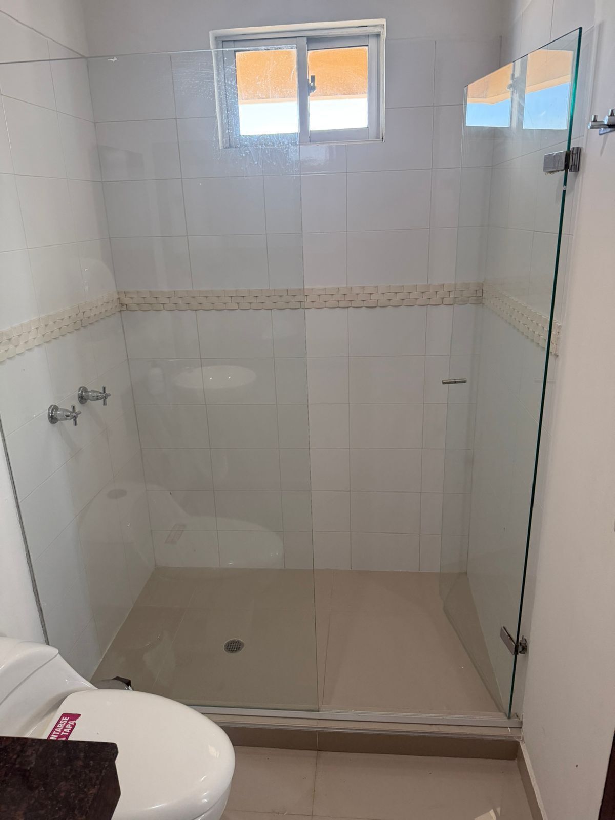 Chuveiro com portas de vidro, uma pequena janela e piso revestido de azulejos.