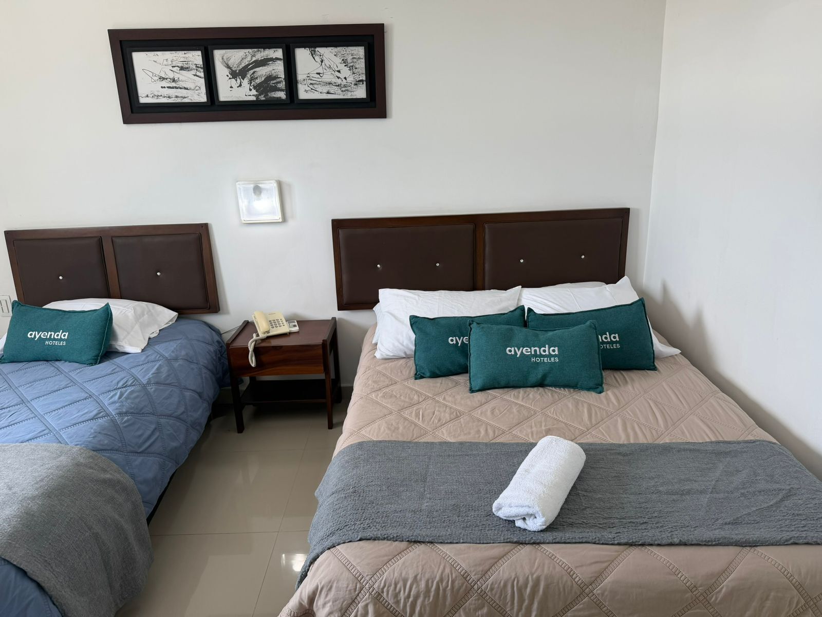 Hotelkamer met twee bedden, elk voorzien van een hoofdeinde, een nachtkastje met een telefoon en kussens met de naam van het hotel.