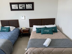 A hotel room with two beds, each with a headboard, a bedside table with a phone, and pillows with the hotel name.