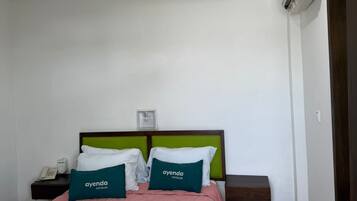 Una habitación de hotel con cama, mesita de noche, teléfono, ventilador de techo y unidad de aire acondicionado.
