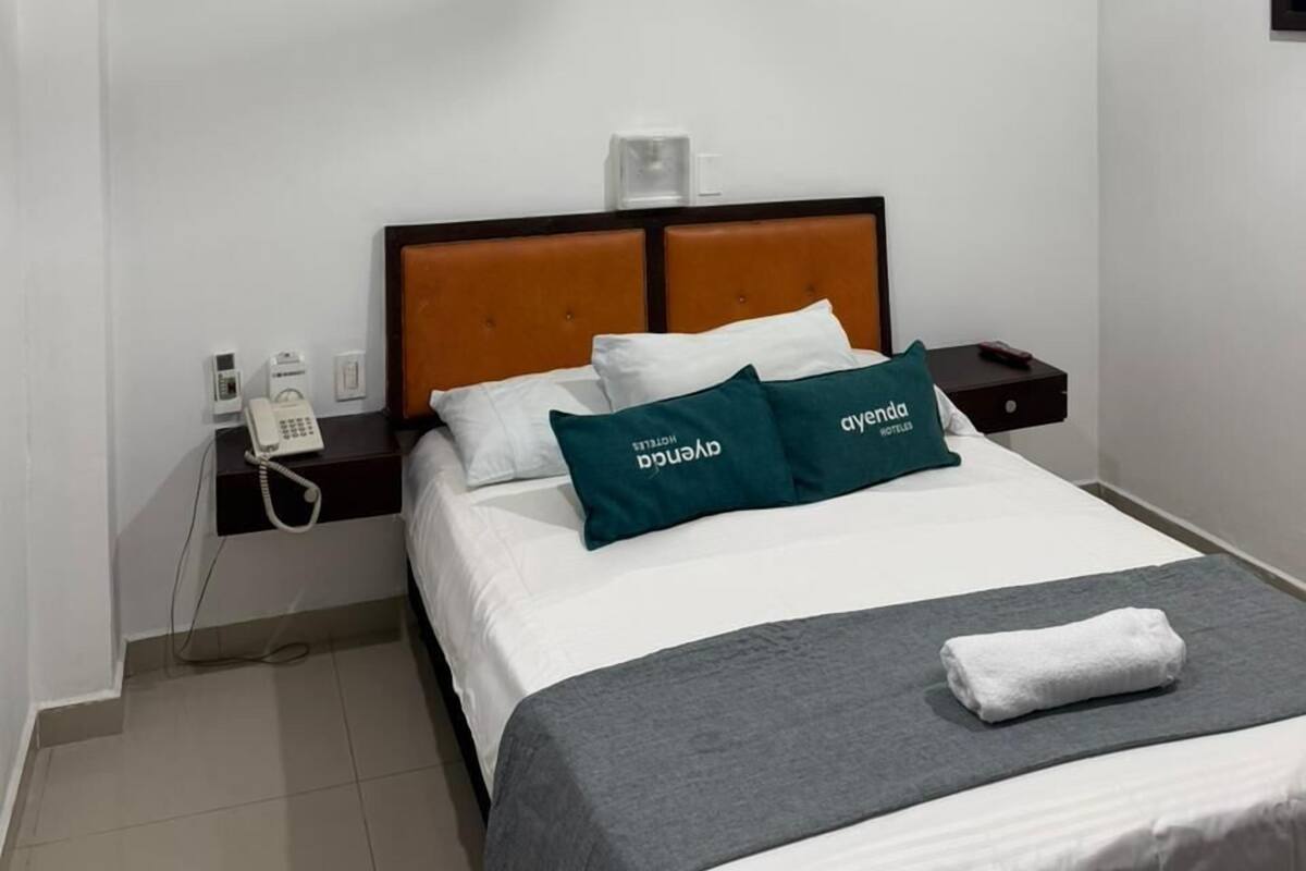 Habitación de hotel con cama, mesita de noche, teléfono, ventilador de techo y aire acondicionado de pared.