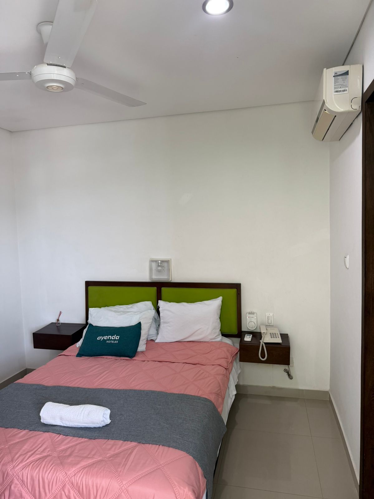 Ein Hotelzimmer mit Bett, Nachttisch, Telefon, Klimaanlage und Deckenventilator.