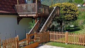 A residential property with a wooden deck, a staircase leading to a balcony, and a paved patio area. - In a house with garden, apartment with terrace near a lake. (Oderen)