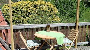 A wooden deck with a table and chairs, a bamboo fence, and a view of houses and greenery in the background. - In a house with garden, apartment with terrace near a lake. (Oderen)