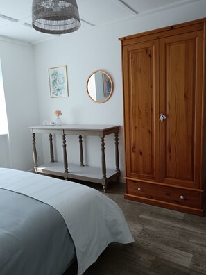 Un dormitorio con una cama, un armario de madera, una mesita de noche con un florero y una lámpara colgante.