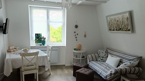 A compact room with a dining table, a sofa, a small ottoman, and a window with a view of greenery. - In a house with garden, apartment with terrace near a lake. (Oderen)