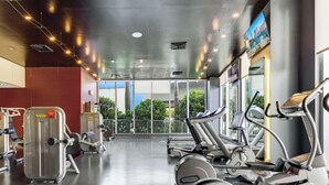 Une salle de sport équipée de machines de cardio, de machines de musculation et dotée d’une grande fenêtre donnant sur un espace verdoyant.