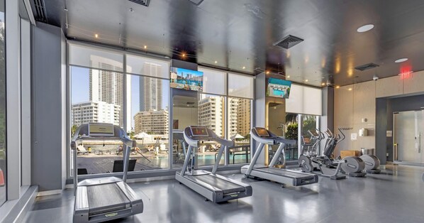 A gym with treadmills and exercise bikes, large windows with a city view, and a modern interior design. - High-Floor 1BR · Intracoastal View · Resort & Pool (Hallandale Beach)