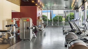 A gym with cardio machines, weight machines, and a large window with a view of greenery. - High-Floor Studio | Intracoastal, Sleeps 4 (Hallandale Beach)