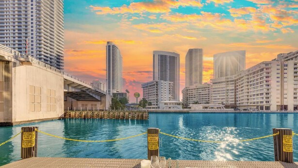A waterfront dining area with a view of the city skyline, a dock, and caution signs. - High-Floor Studio | Intracoastal, Sleeps 4 (Hallandale Beach)