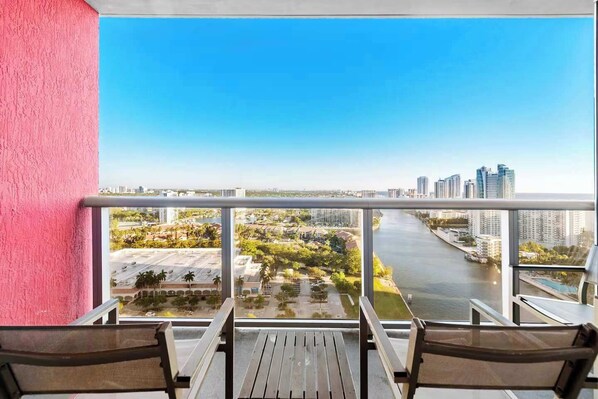 A balcony with a view of a river, cityscape, and a pink wall. - High-Floor Studio | Intracoastal, Sleeps 4 (Hallandale Beach)