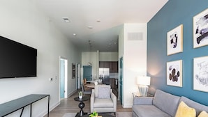 Ein modernes Wohnzimmer mit Flachbildfernseher, Couchtisch mit Dekoration, Sofa mit Kissen und Kunstwerken an den Wänden.