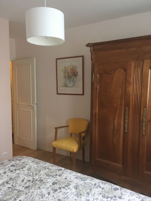 A room with a bed, a wooden wardrobe, a yellow chair, a white door, and a framed picture on the wall.