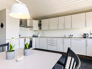 A modern kitchen with white cabinets, a white table, and a hanging light fixture. - 4 Person Holiday Park Home in Karrebaeksminde (Karrebæksminde)