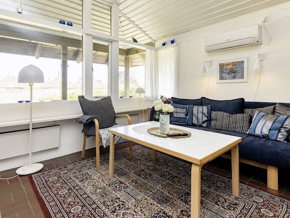 A room with a sofa, a table, a chair, a patterned rug, and a window with curtains. - 4 Person Holiday Park Home in Karrebaeksminde (Karrebæksminde)
