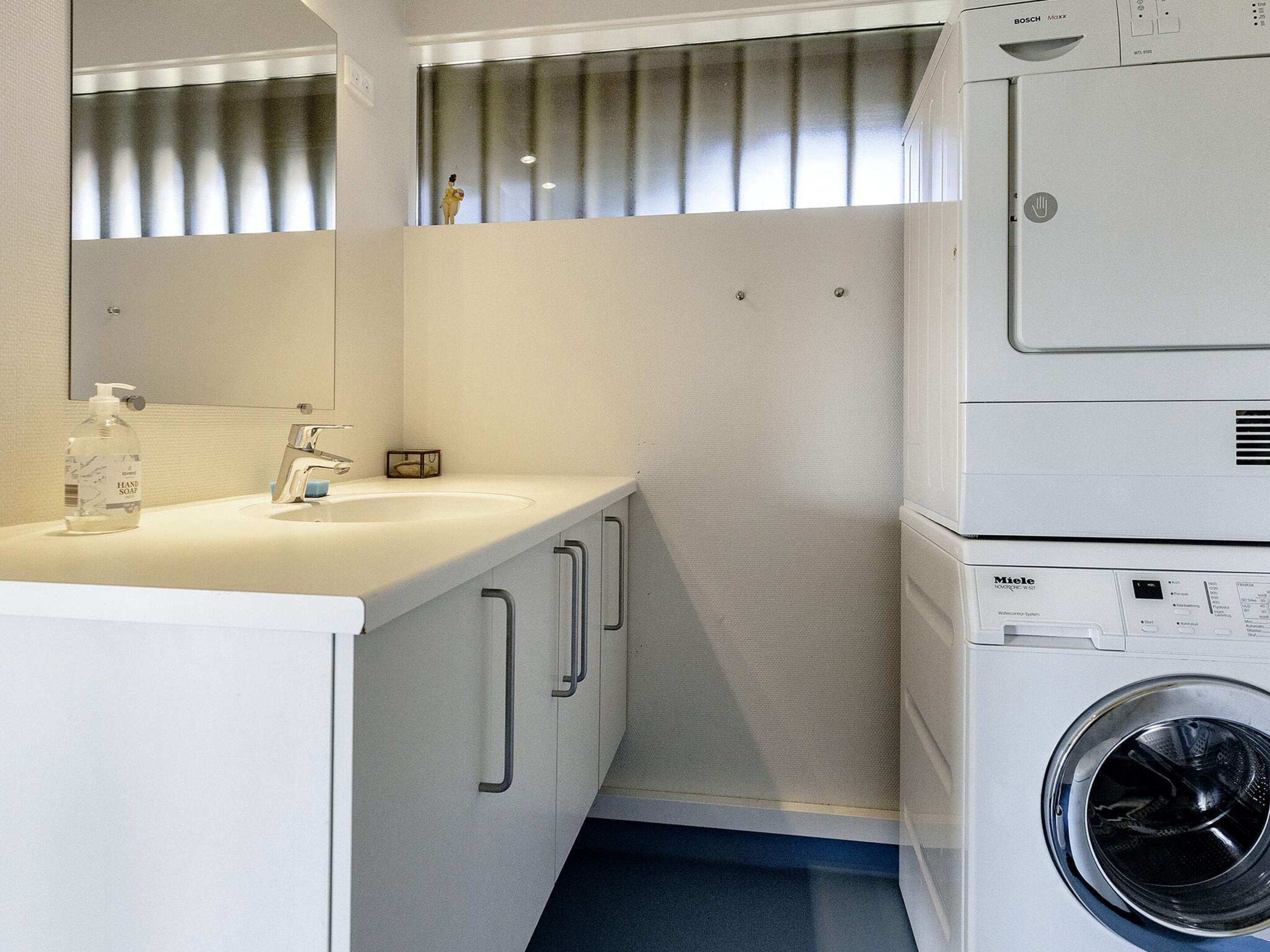A compact, modern bathroom with a sink, mirror, and stacked washing machine.