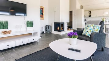 Ett modernt vardagsrum med en platt-TV, en öppen spis, en soffa med mönstrade kuddar och ett soffbord med en fjärrkontroll.