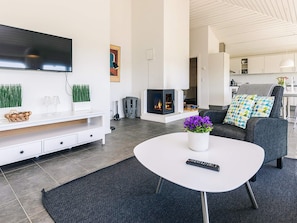 A modern living room with a flat-screen TV, a fireplace, a sofa with patterned cushions, and a coffee table with a remote control.