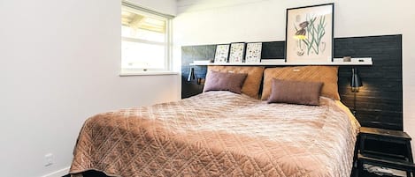 A bedroom with a bed, a window, a headboard, and wall art.