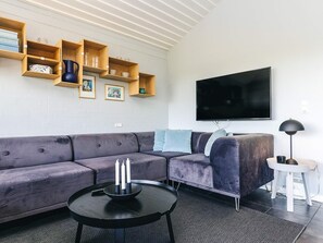 A modern living room with a sectional sofa, a flat-screen TV, wooden shelves, and a small side table.